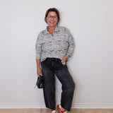Person wearing a patterned shirt, dark jeans, and red shoes against a white wall.