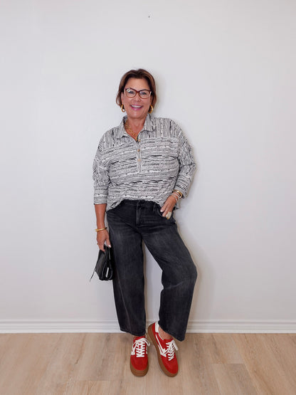 Person wearing a patterned shirt, dark jeans, and red shoes against a white wall.