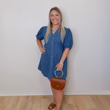 Woman wearing a blue dress standing against a white wall.