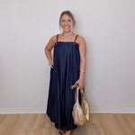 Woman in a navy dress holding a gold handbag against a white wall.
