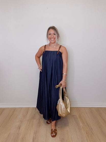 Woman in a navy dress holding a gold handbag against a white wall.