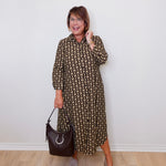 Woman wearing a patterned dress holding a handbag against a white wall.