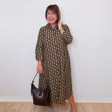 Woman wearing a patterned dress holding a handbag against a white wall.