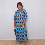 Woman wearing a blue patterned dress against a white wall