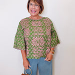 Woman wearing a patterned top and jeans, holding a brown handbag against a white background