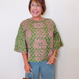 Woman wearing a patterned top and jeans, holding a brown handbag against a white background