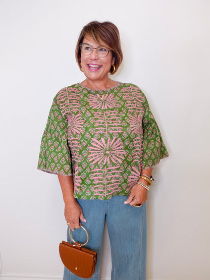 Woman wearing a patterned top and jeans, holding a brown handbag against a white background