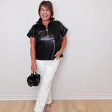Woman wearing a black leather top and white pants against a plain background