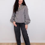 Woman wearing a patterned top and black pants against a white wall