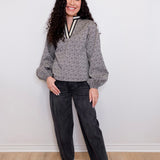 Woman wearing a patterned top and black pants against a white wall
