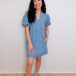 Woman wearing a blue dress standing against a white wall.