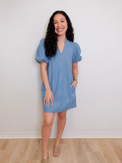 Woman wearing a blue dress standing against a white wall.