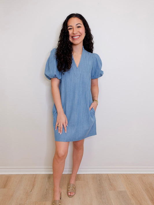 Woman wearing a blue dress standing against a white wall.