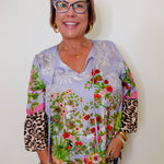 Woman wearing a colorful floral and leopard print blouse against a white background