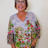 Woman wearing a colorful floral and leopard print blouse against a white background