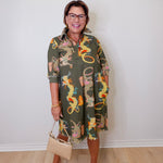 Woman wearing a patterned dress with dragons, holding a beige handbag indoors.