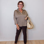 Woman wearing a beige top and black pants, holding a gold handbag against a white wall.