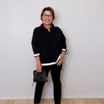 Woman wearing a black outfit with white trim against a plain wall.
