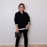 Woman wearing a black outfit with white trim against a plain wall.