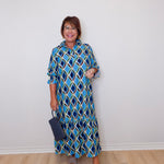 Woman wearing a blue patterned dress against a white wall.