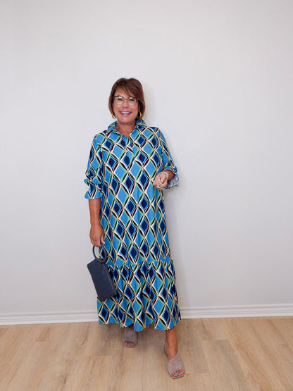 Woman wearing a blue patterned dress against a white wall.