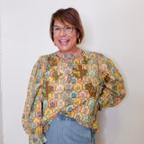 Woman wearing a patterned blouse and jeans against a white wall