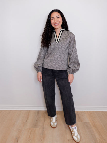 Woman wearing a gray sweater with a V-neck and dark jeans, standing against a white wall.