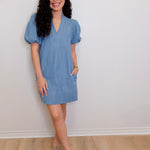 Woman wearing a blue dress standing against a white wall.