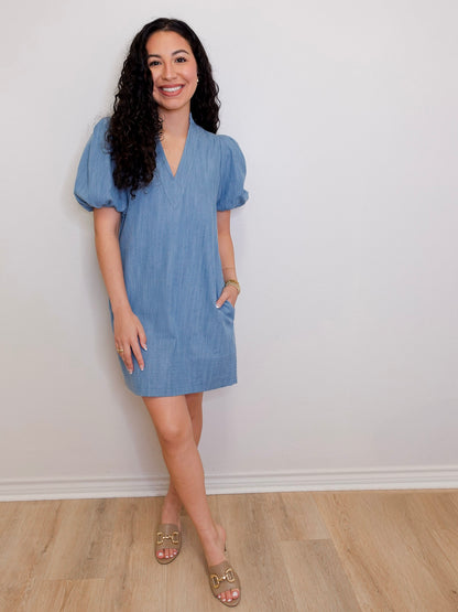 Woman wearing a blue dress standing against a white wall.