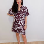 Woman wearing a maroon and white tie-dye dress against a plain white wall.