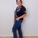Woman wearing a black floral top and blue jeans against a white wall.