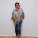 Woman wearing a colorful floral blouse with leopard print accents and blue jeans against a white wall.