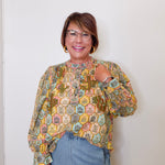 Woman wearing a patterned blouse and blue jeans against a white wall