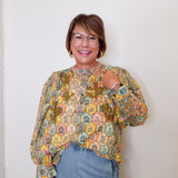 Woman wearing a patterned blouse and blue jeans against a white wall