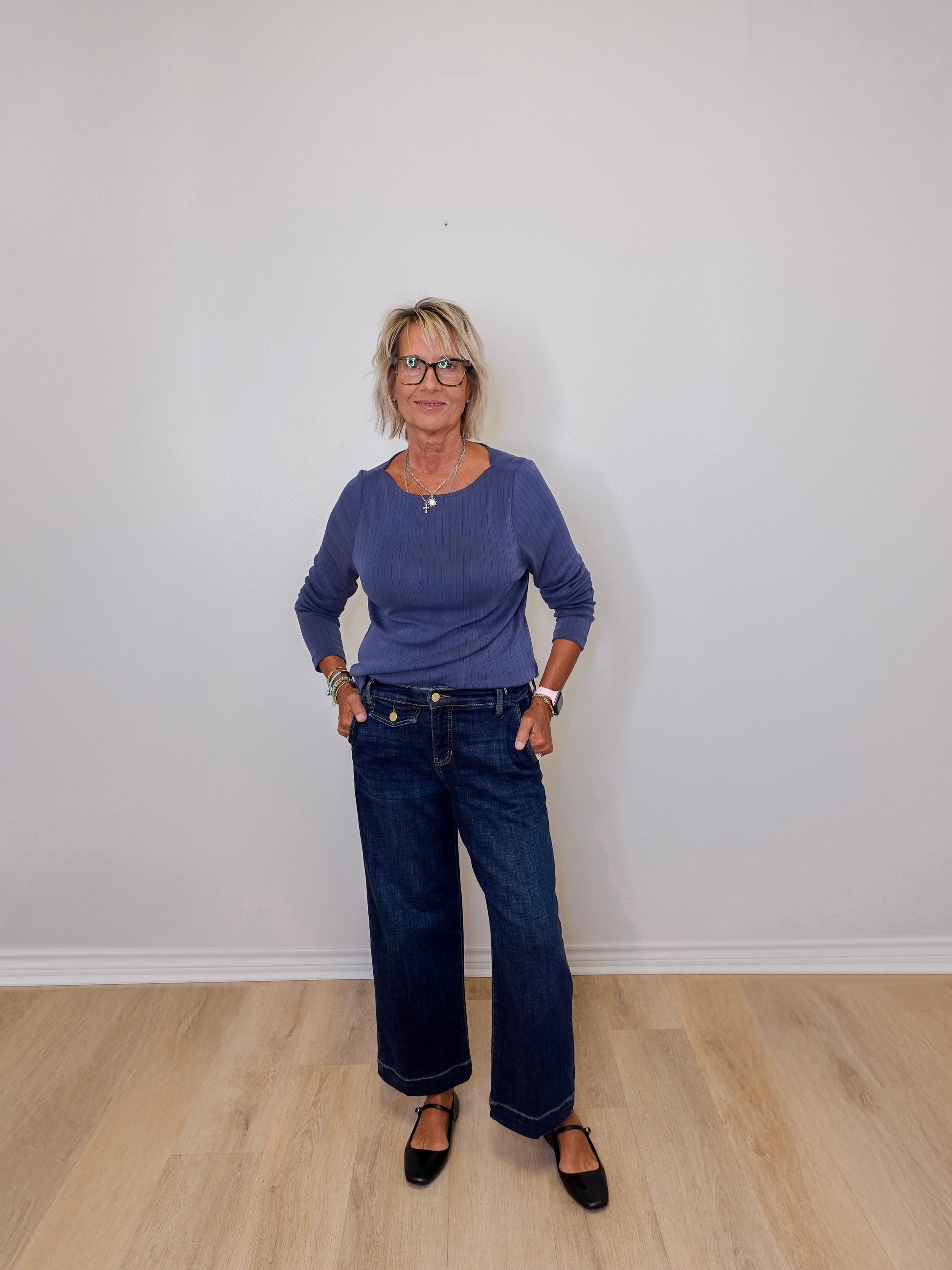 Woman wearing a purple sweater and blue jeans standing against a plain white wall.
