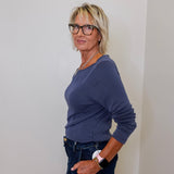 Woman wearing a blue top and dark jeans against a white wall