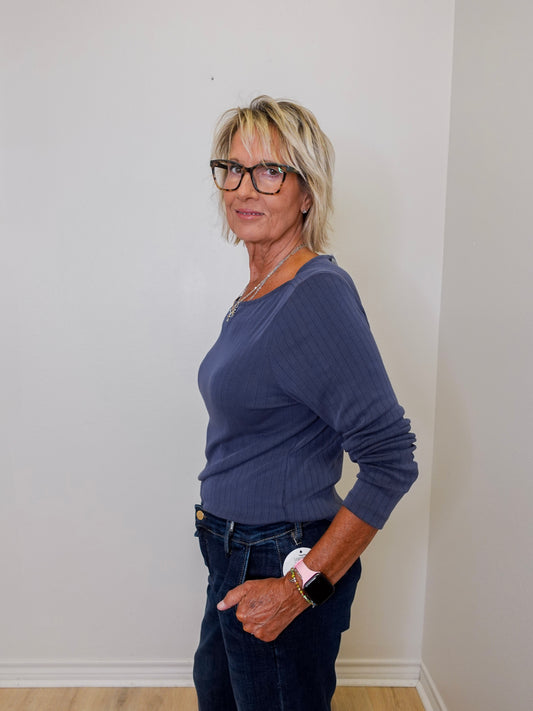 Woman wearing a blue top and dark jeans against a white wall