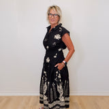 Woman wearing a black floral dress against a white wall