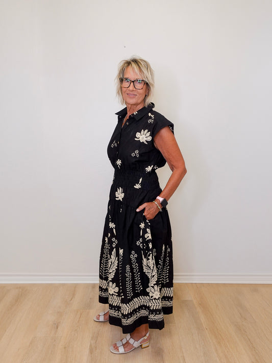 Woman wearing a black floral dress against a white wall