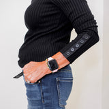Person wearing a black ribbed sweater with button details on the sleeves, paired with blue jeans.
