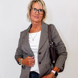 Woman wearing a brown  blazer, white shirt, and jeans with a handbag against a plain background