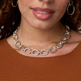 Close-up of a person wearing a silver chain necklace with a brown top.