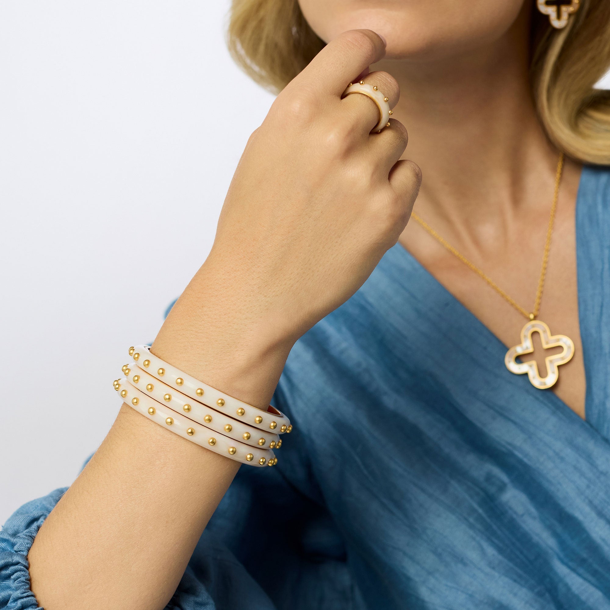 Woman wearing a gold bracelet, ring, and necklace on a light background