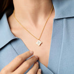 Gold necklace with a floral pendant worn by a person in a light blue shirt.