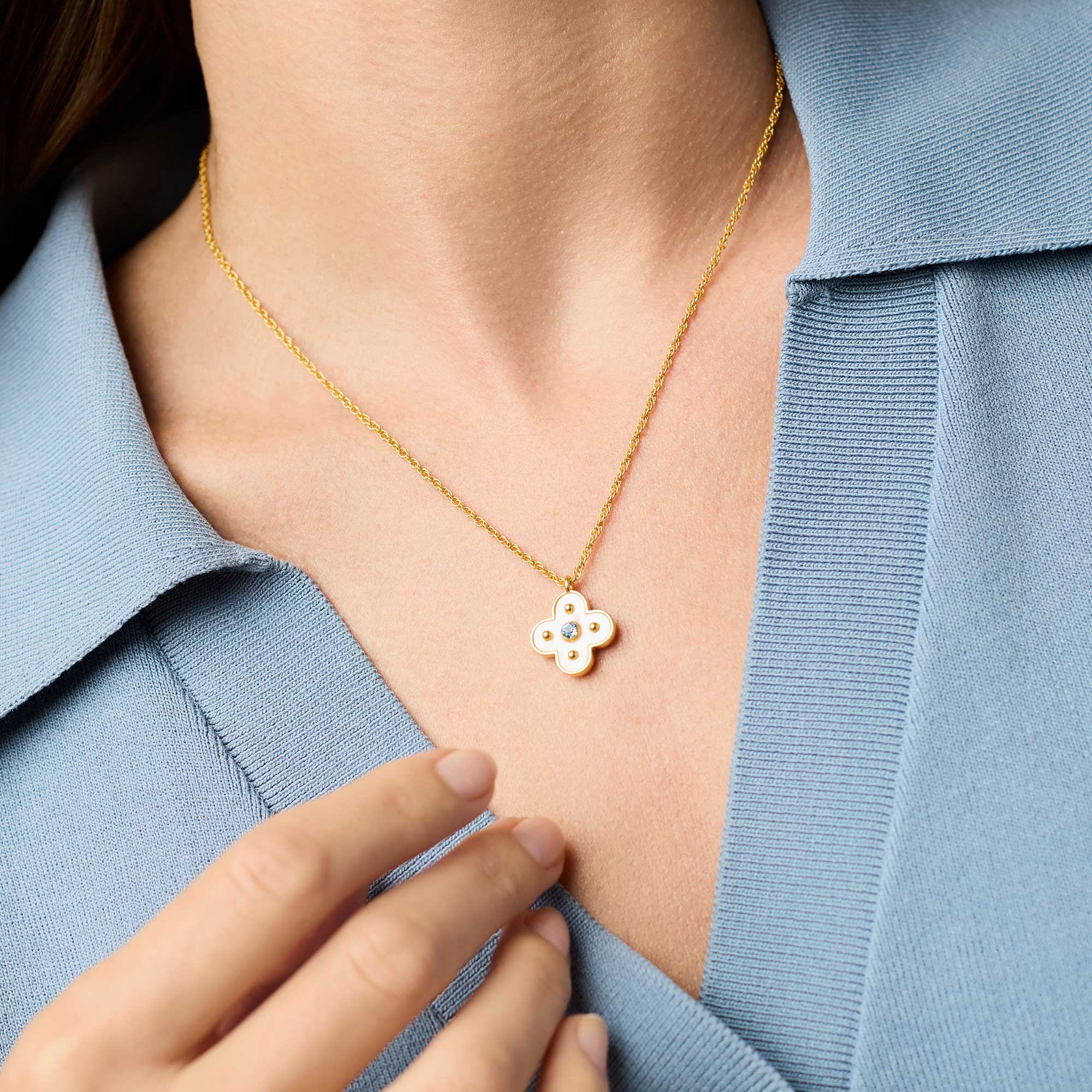 Gold necklace with a floral pendant worn by a person in a light blue shirt.