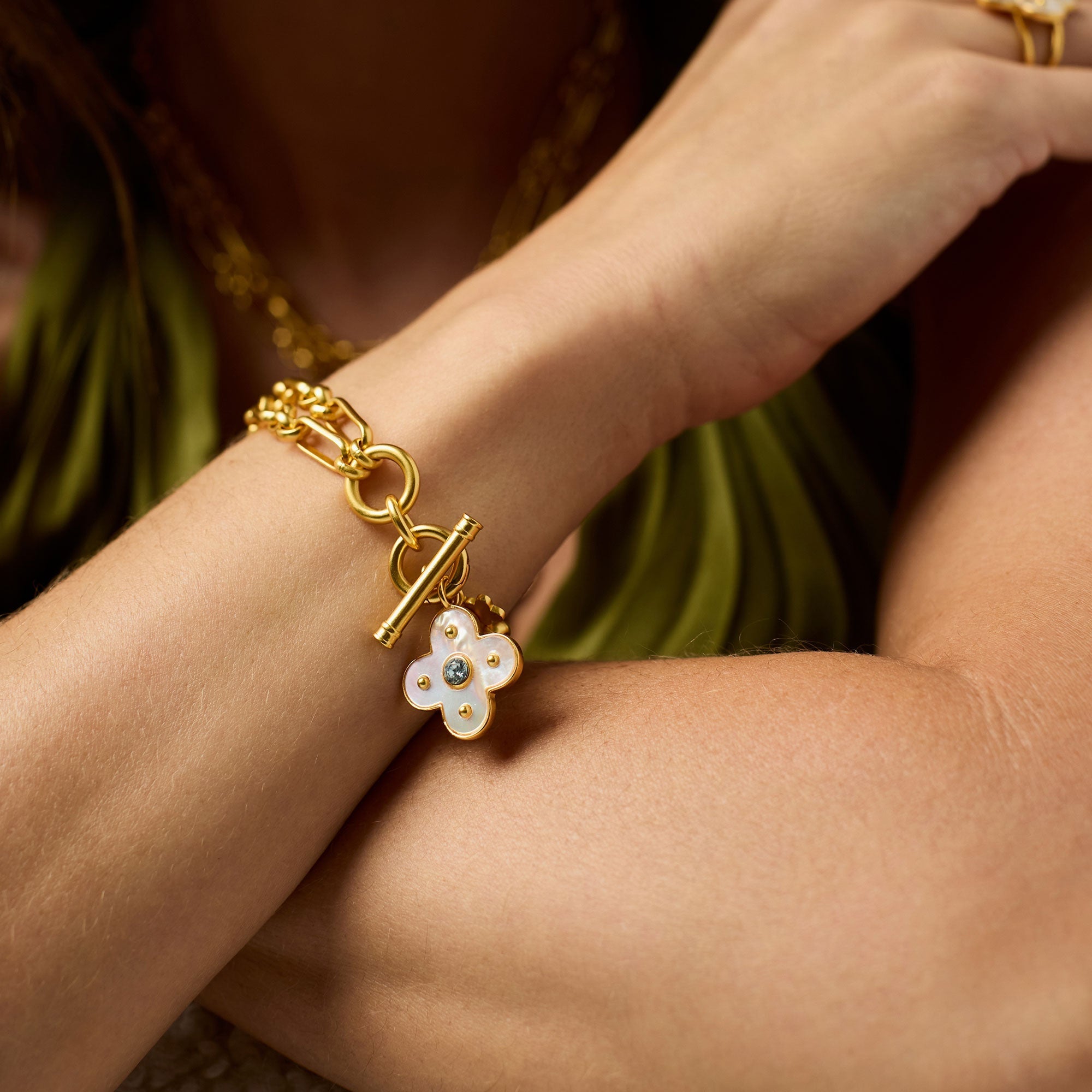 model wearing Gold bracelet with a floral charm on it 