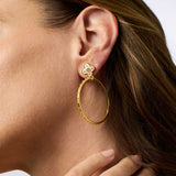 Gold hoop earring with floral detail worn by a person