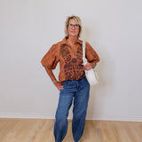 Woman wearing a patterned shirt, jeans, and white sneakers against a plain wall.