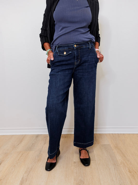 Person wearing dark blue jeans and a black top against a white wall.