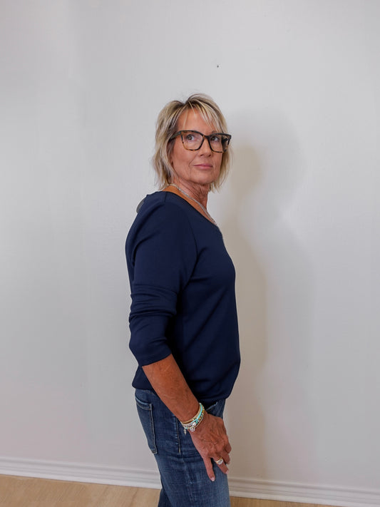 Person wearing a navy blue sweater and jeans standing against a white wall.